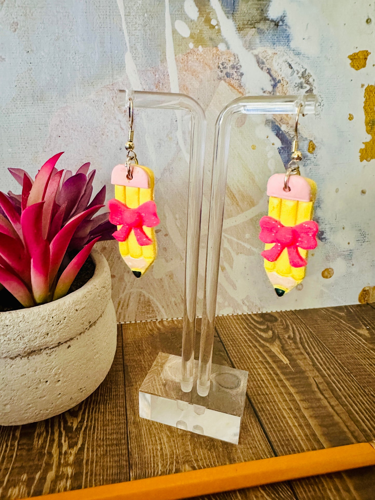 Straight polymer clay pencil earring on earring stand, wooden table, colorful wall and succulent backdrop.