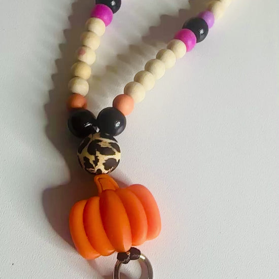 Video demonstration showcasing three different Halloween themed beaded lanyards with various color schemes and charm combinations, featuring the trick or treat lanyard as the second item displayed, showing movement and bead details.