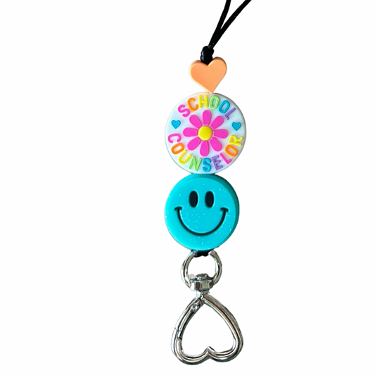 Close-up of school counselor lanyard showing smiley face focal bead, flower bead, and heart-shaped clasp on white background