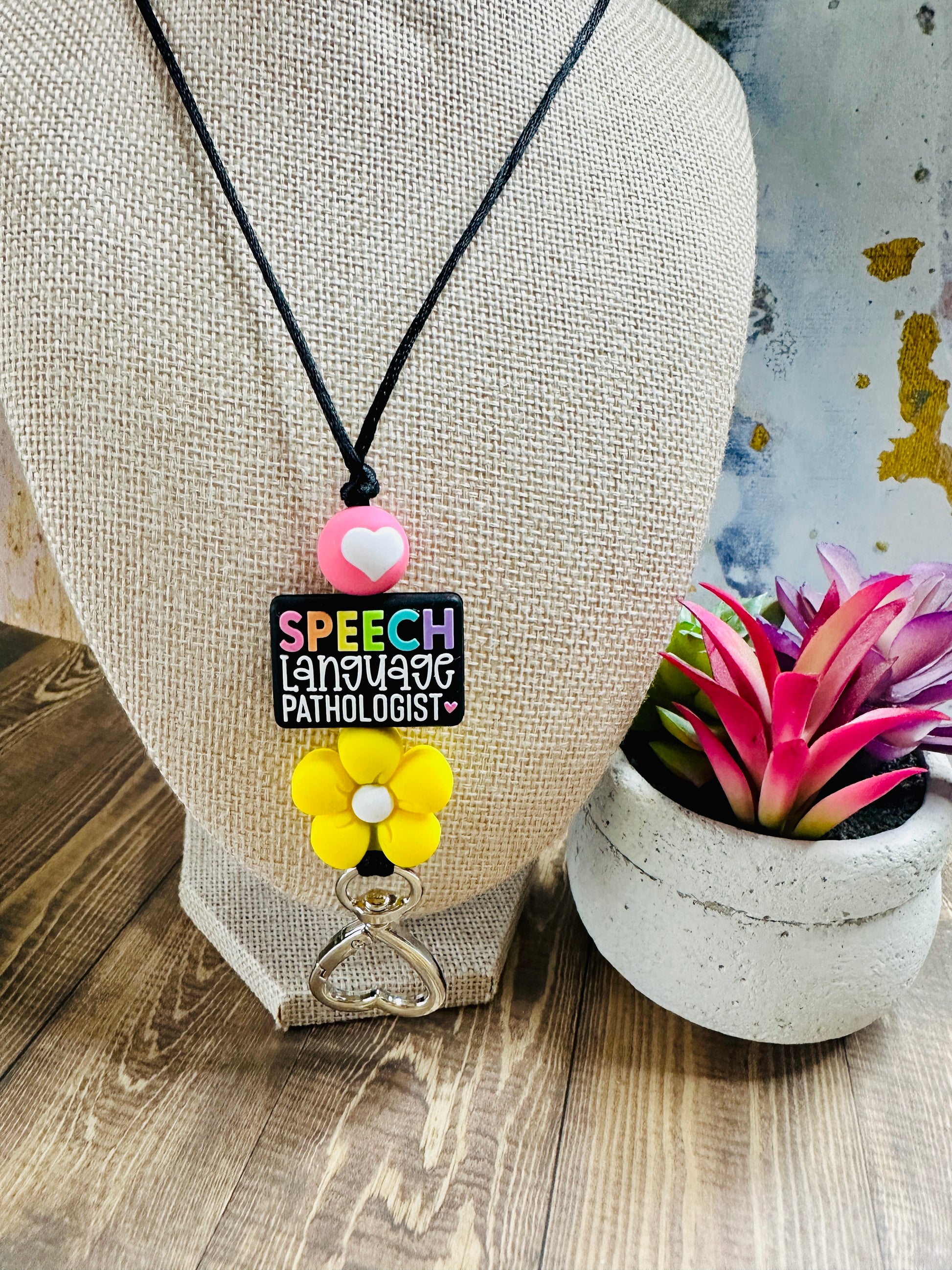 Speech language pathologist lanyard hanging on grey mannequin with small potted succulent, showing colorful bead detail.