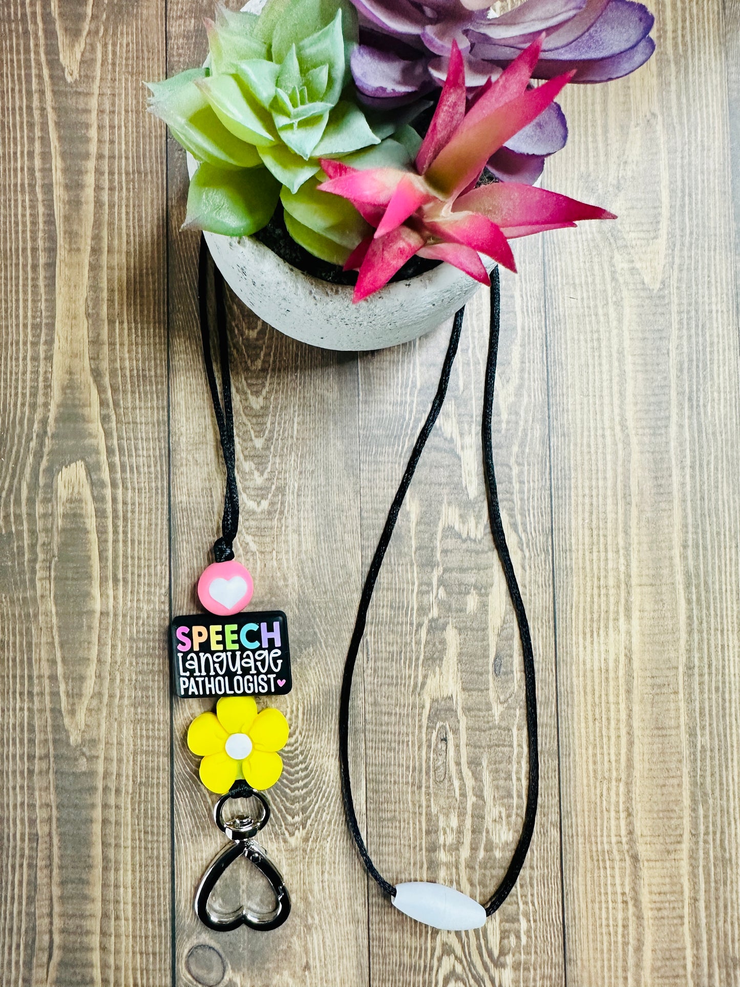 Full view of SLP lanyard displayed on wooden table with small potted succulent, showing black nylon cord and colorful silicone beads.