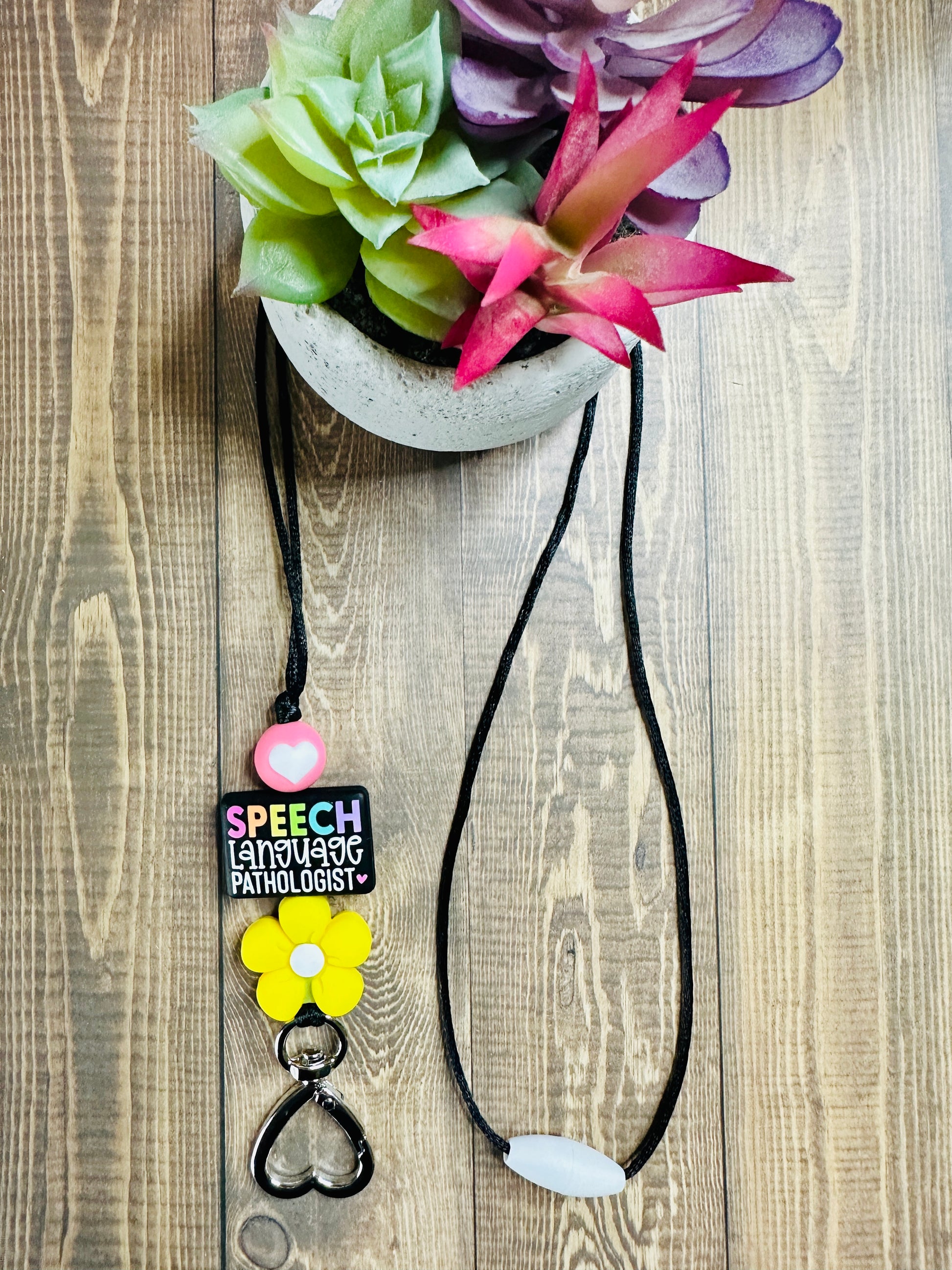 Full view of SLP lanyard displayed on wooden table with small potted succulent, showing black nylon cord and colorful silicone beads.