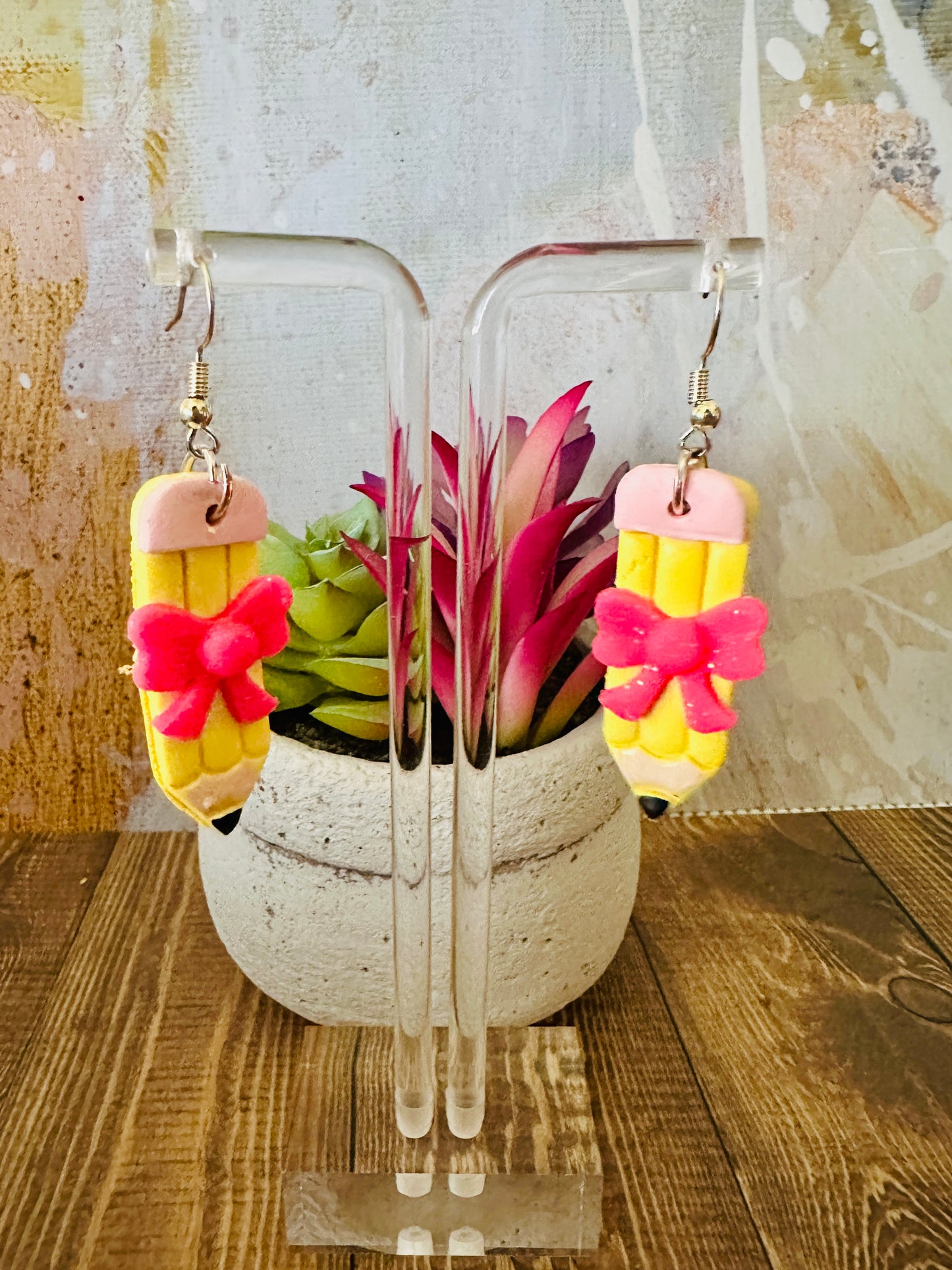 Handmade straight pencil earring on wooden earring stand with colorful wall and potted succulent in background.