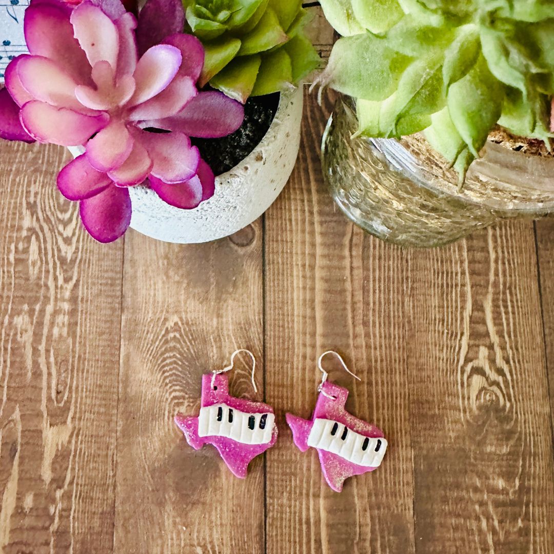 Purple Texas piano-shaped earrings on a wooden surface with plants in the background