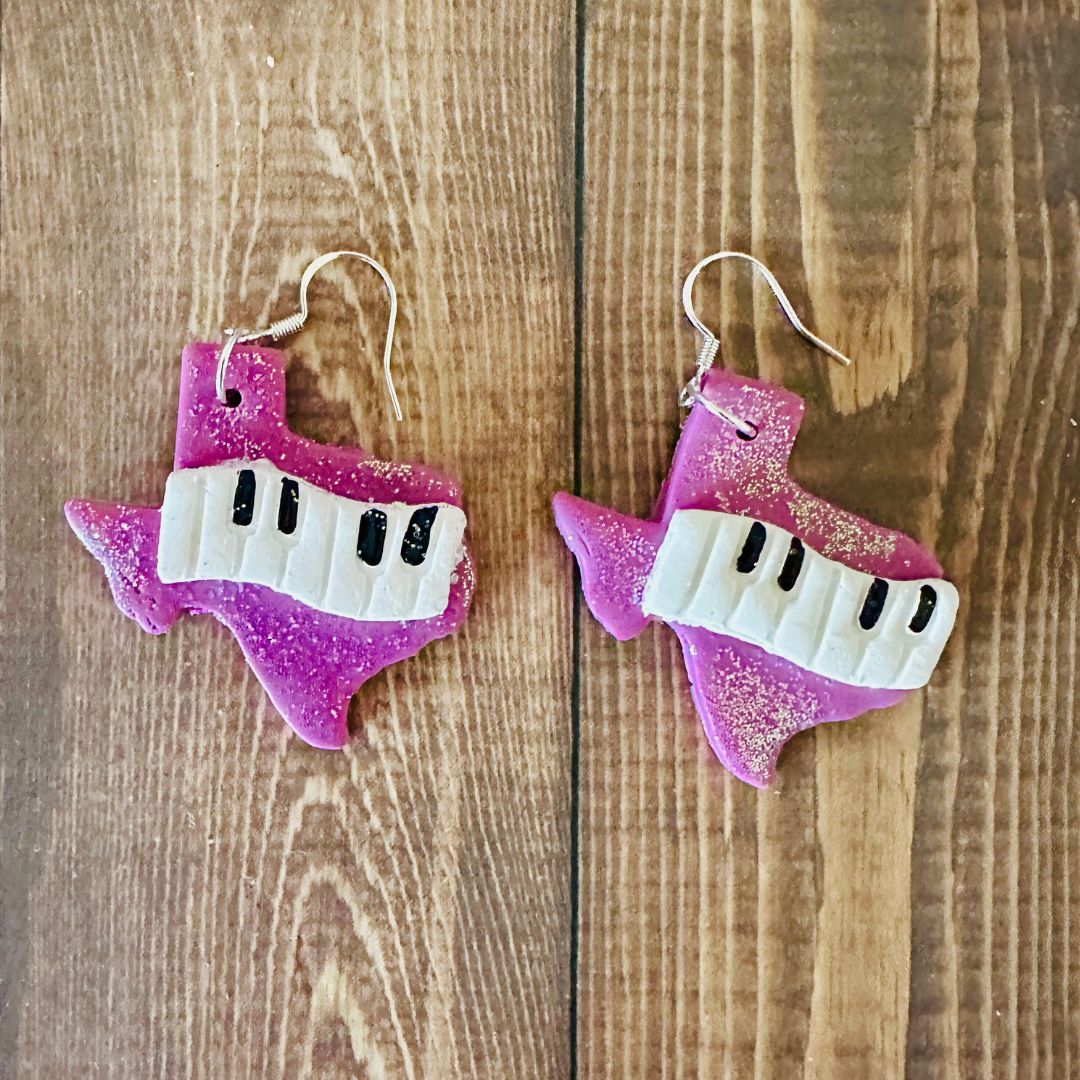 Purple and white Texas keyboard-shaped earrings on a wooden surface