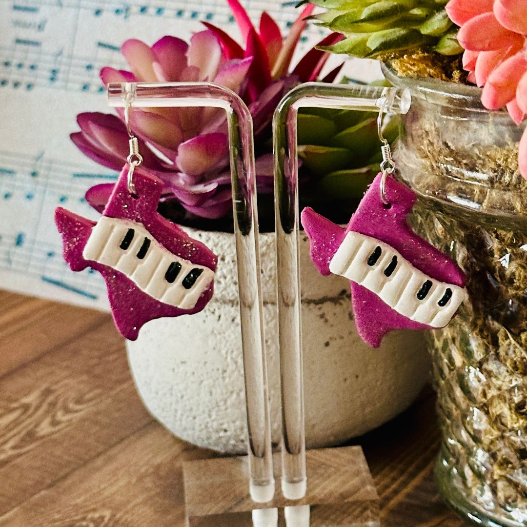 Purple and white Texas keyboard-shaped earrings on a clear stand with a floral background.